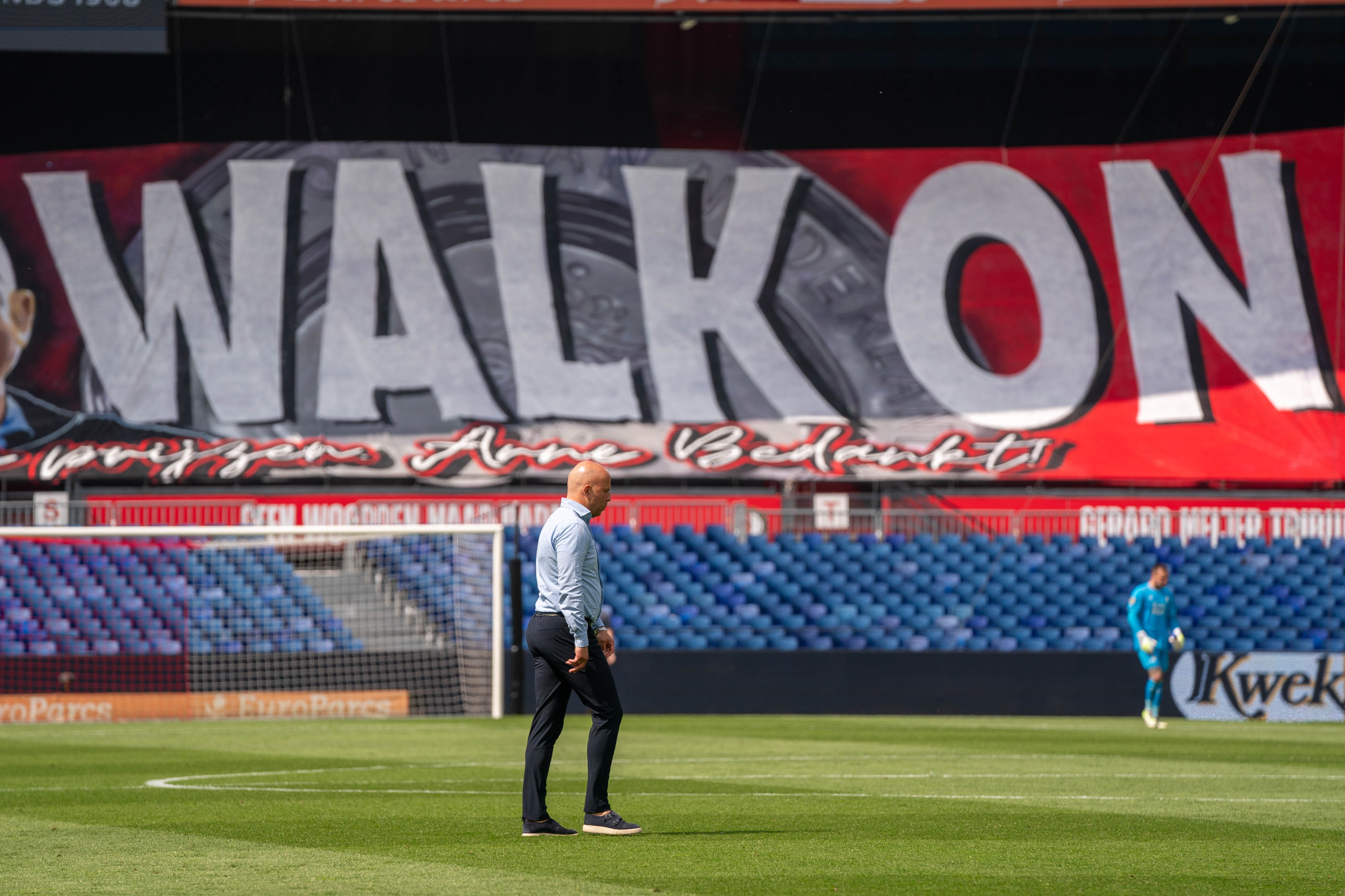 Arne Slot loopt over het veld van De Kuip, met op de achtergrond een speciaal spandoek voor de coach